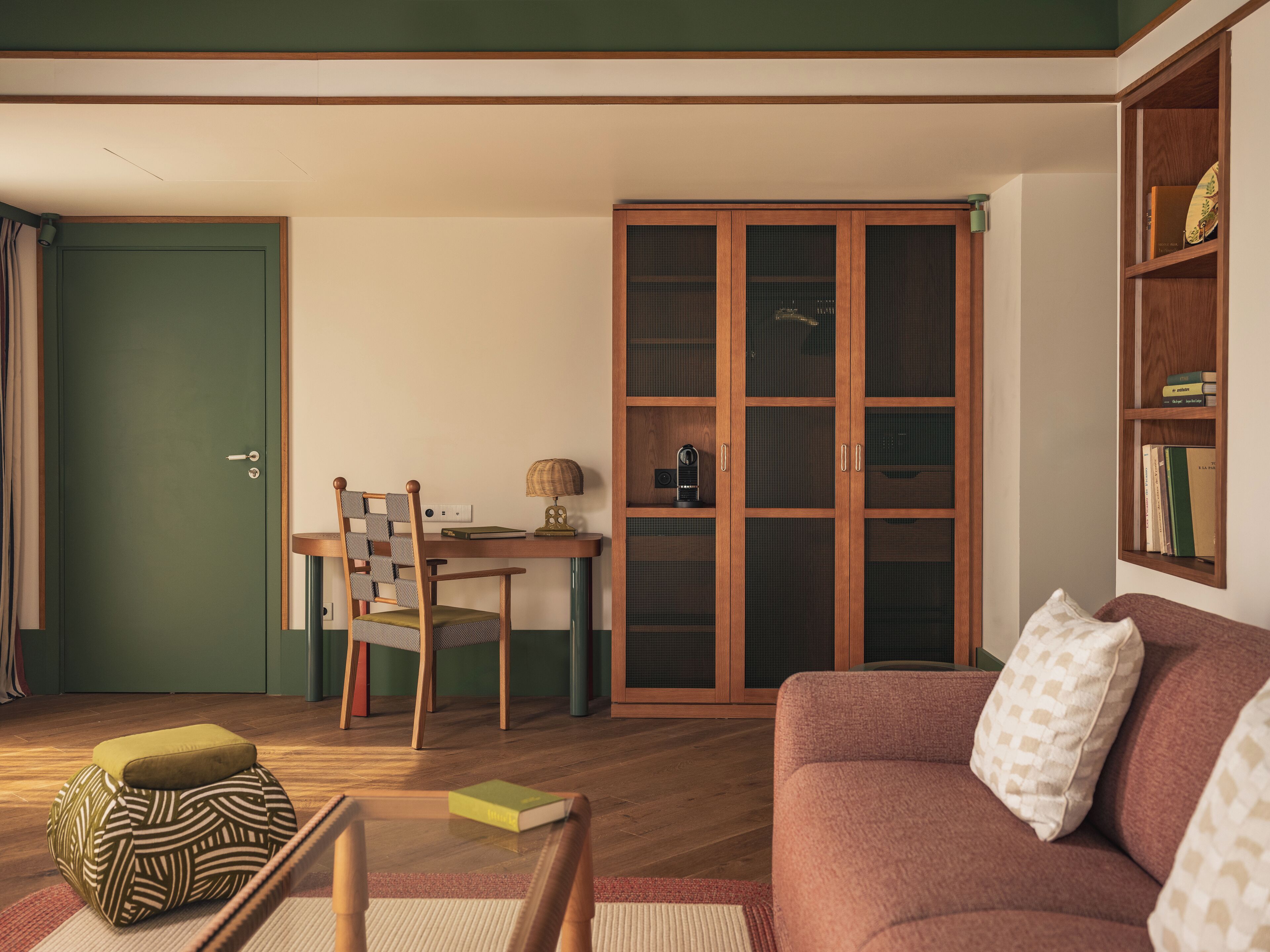 A cozy living room with a sofa, a dining table with chairs, a bookshelf, and a green door.