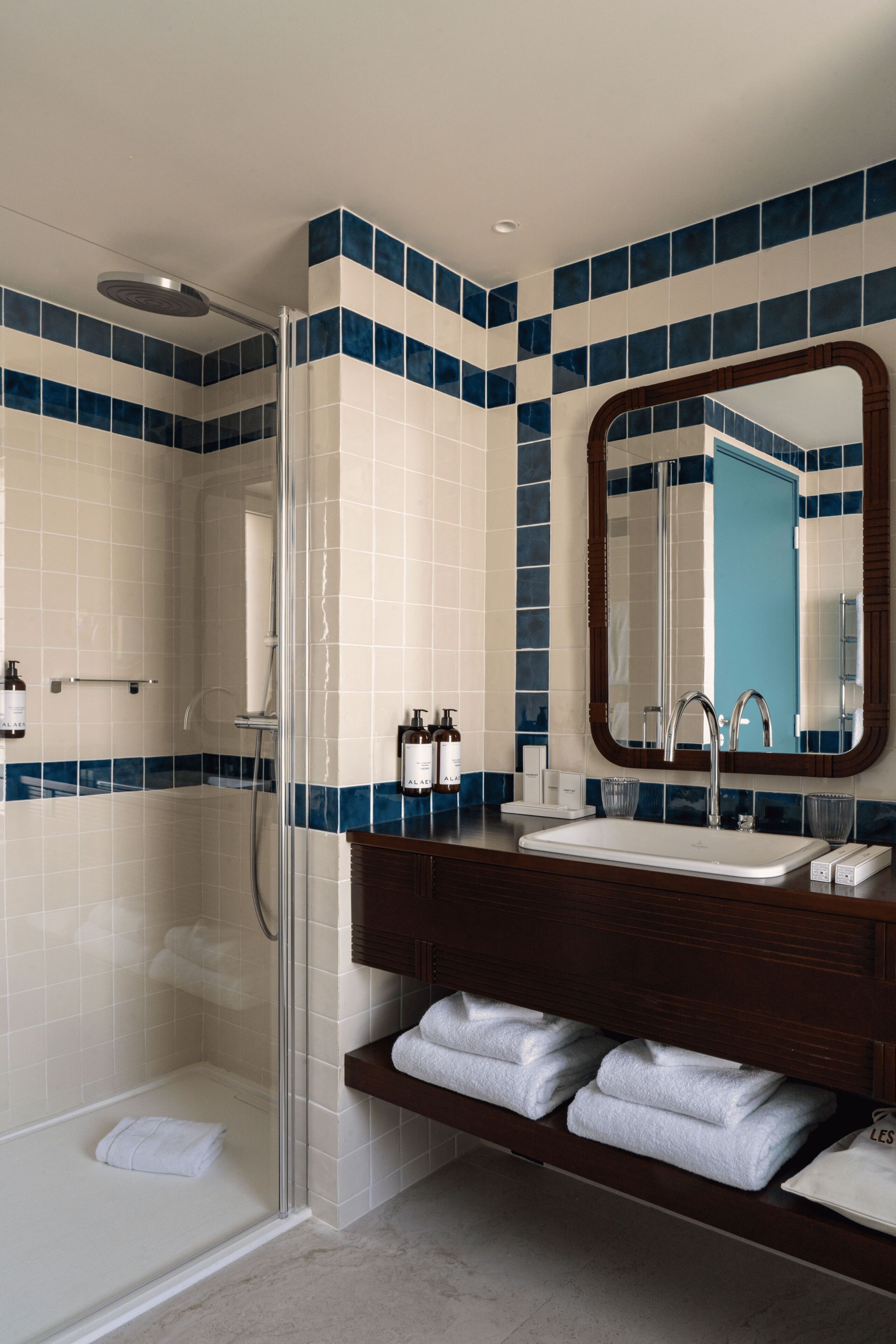 A modern bathroom with a glass-enclosed shower, a wooden vanity with a mirror, and a white sink.