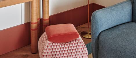 A room with a wooden side table, a floor lamp, a sofa, and a patterned ottoman.