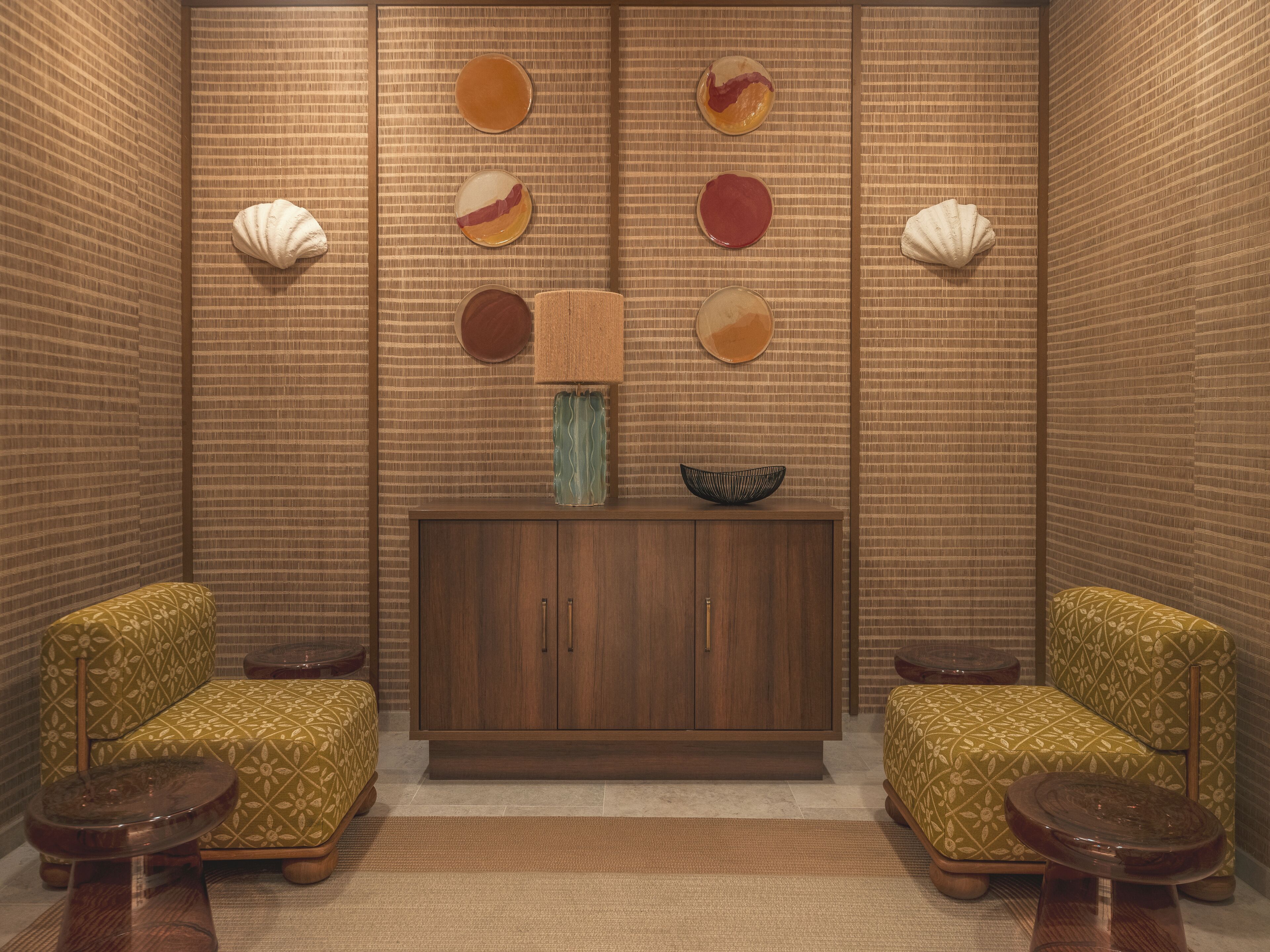 A room with a patterned wall, a wooden cabinet, two patterned armchairs, and a small table.