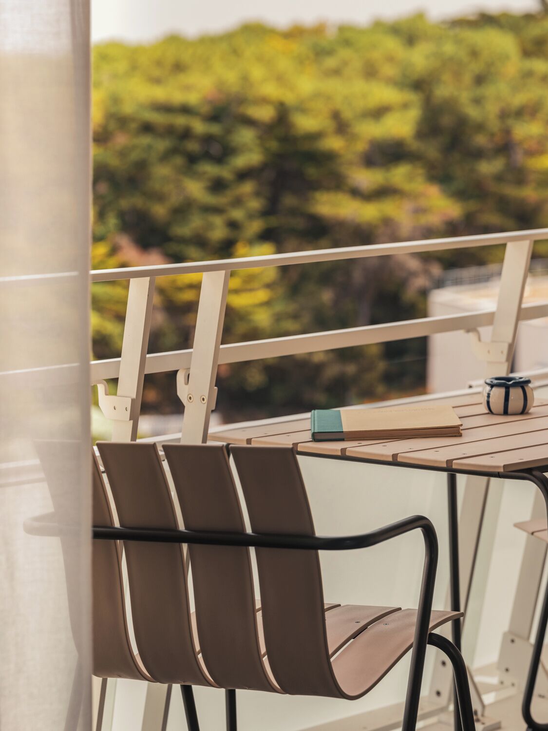 A balcony with a table and chairs, a book, and a mug.