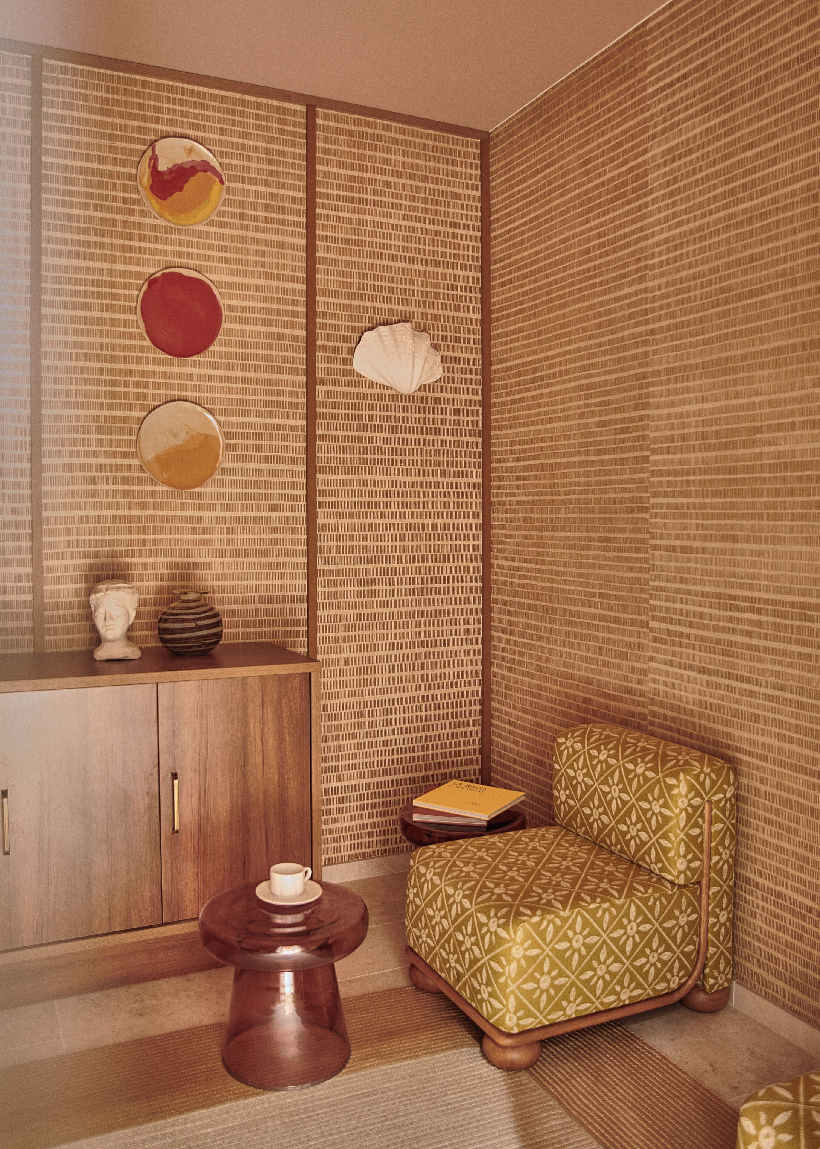 A room with a patterned wall, a wooden cabinet, a small round table with a cup, and a patterned armchair.