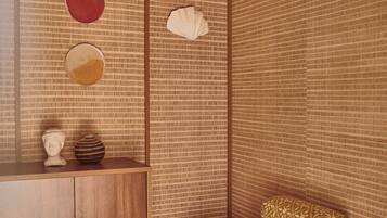 A room with a patterned wall, a wooden cabinet, a small round table with a cup, and a patterned armchair.