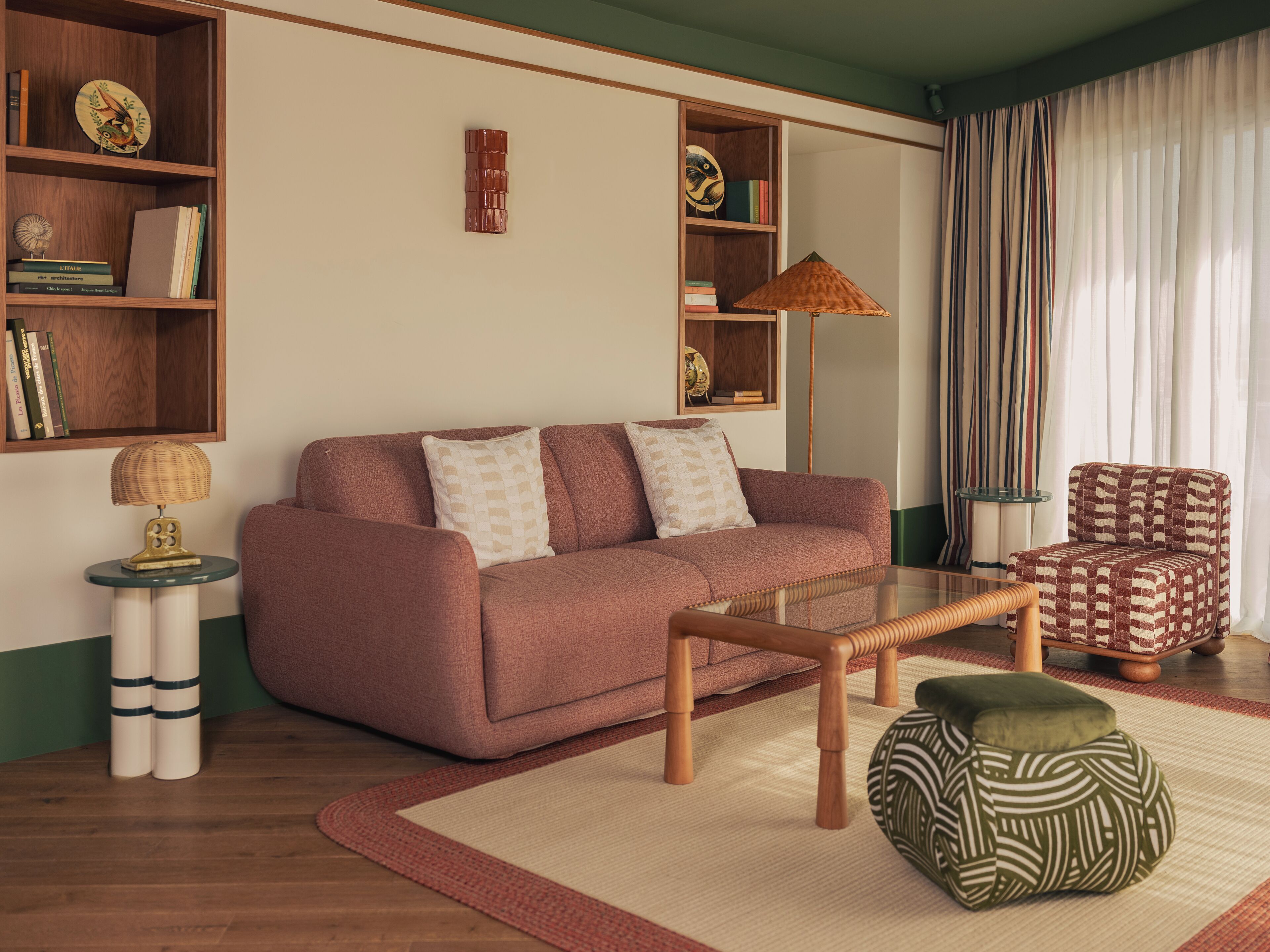A living room with a sofa, a coffee table, a patterned ottoman, a lamp, and bookshelves.
