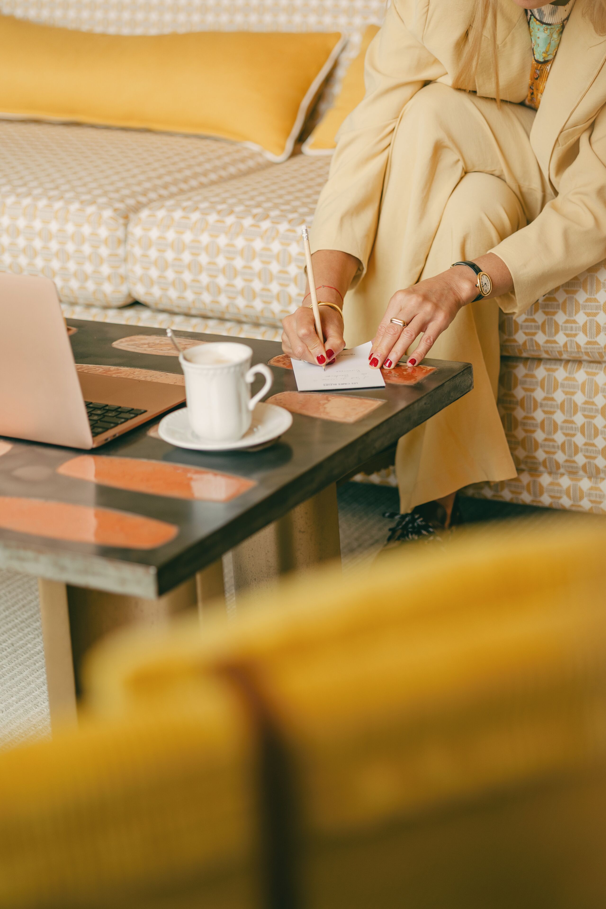 A person sitting at a table with a laptop, writing on a piece of paper, and a cup of coffee.