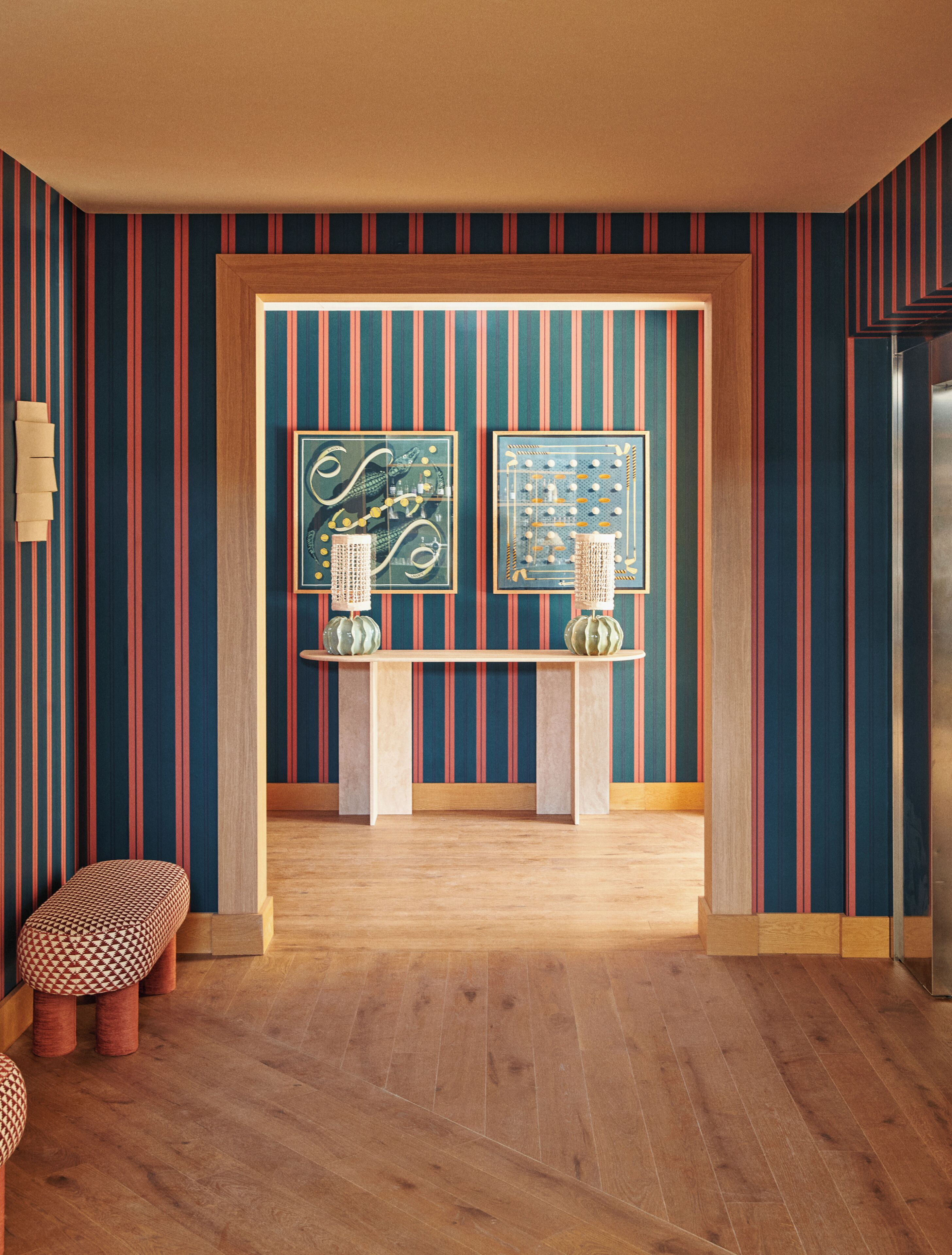 Un intérieur moderne avec un papier peint à rayures, un banc en bois et deux œuvres d’art encadrées accrochées à un mur.