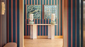 Un intérieur moderne avec un papier peint à rayures, un banc en bois et deux œuvres d’art encadrées accrochées à un mur.