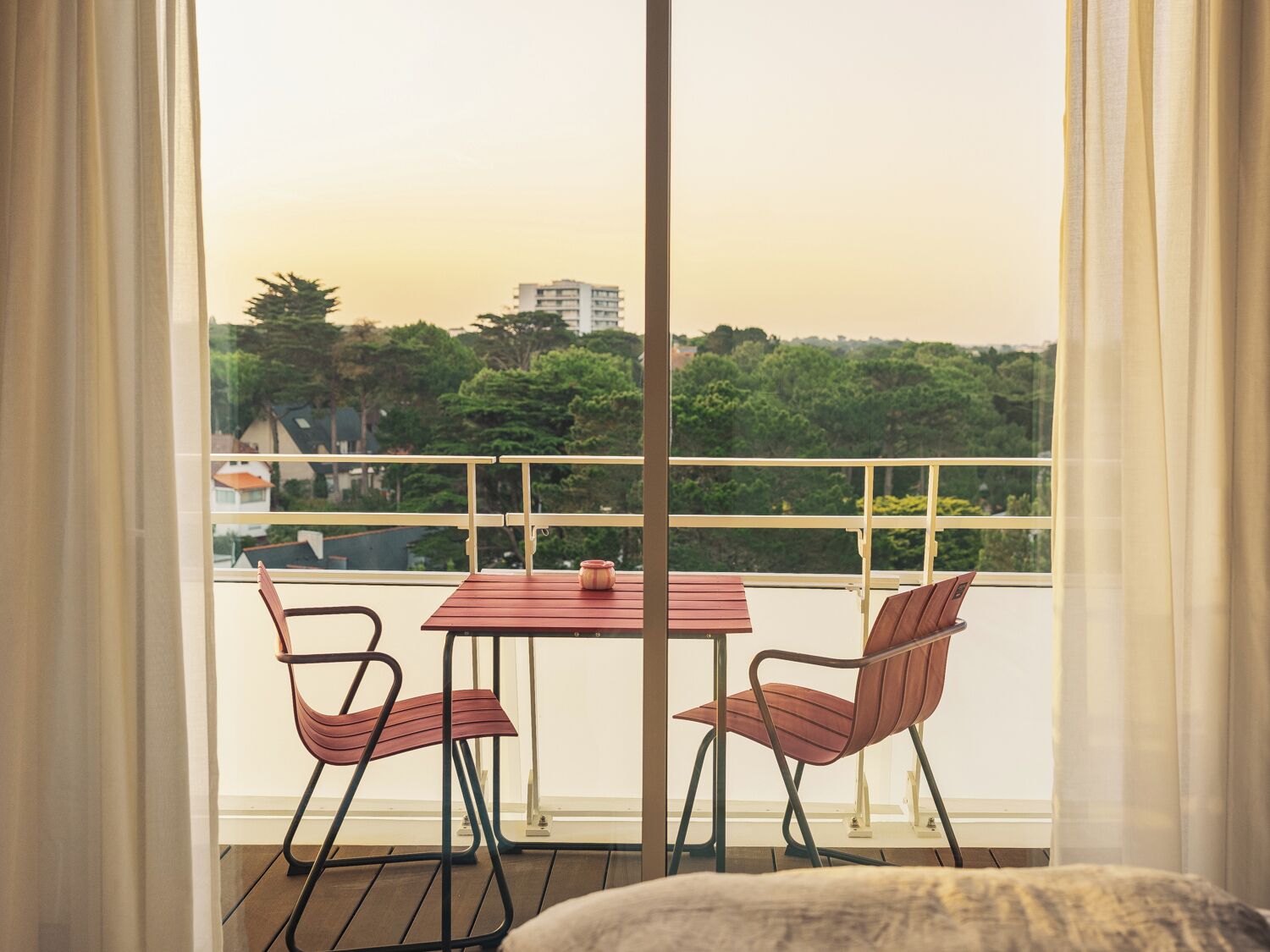 A balcony with a table and two chairs, a view of a cityscape, and a railing.
