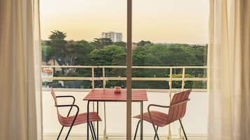 A balcony with a table and two chairs, a view of a cityscape, and a railing.