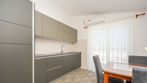 Eine moderne Küche mit grauen Schränken, einer Edelstahlspüle und einem Essbereich mit einem Holztisch und zwei Stühlen.