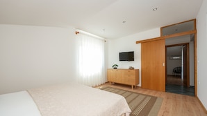 Ein Schlafzimmer mit einem Bett, einem Holzschrank, einem Fernseher und einer Tür zu einem anderen Raum.
