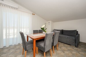 Ein Essbereich mit Holztisch und grau gepolsterten Stühlen, einem grauen Sofa und einer Topfpflanze.