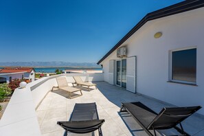 Eine Dachterrasse mit Meerblick, ausgestattet mit zwei Liegestühlen und einem Tisch.