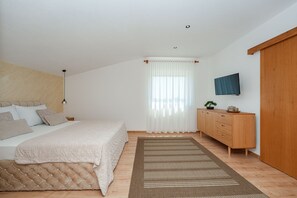 Une chambre à coucher comprenant un lit, une armoire en bois, un téléviseur fixé au mur et une fenêtre ornée de rideaux légers.