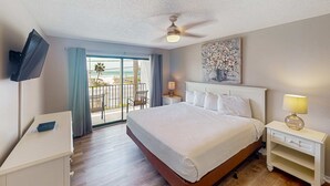 A hotel room with a bed, a desk, a TV, a ceiling fan, a painting, and a balcony with a view. - Golf lovers’s condo with golf, 11 pools, hot tubs, gym, tennis, pickleball, W/D (Panama City Beach)