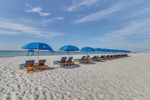 Een strand met rijen houten ligstoelen en blauwe parasols, netjes op een rij langs de kust.