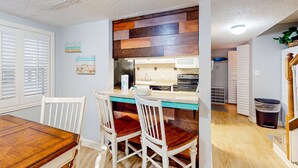 Une cuisine avec un revêtement mural en bois, des armoires blanches et un coin repas comprenant une table en bois et des chaises blanches.