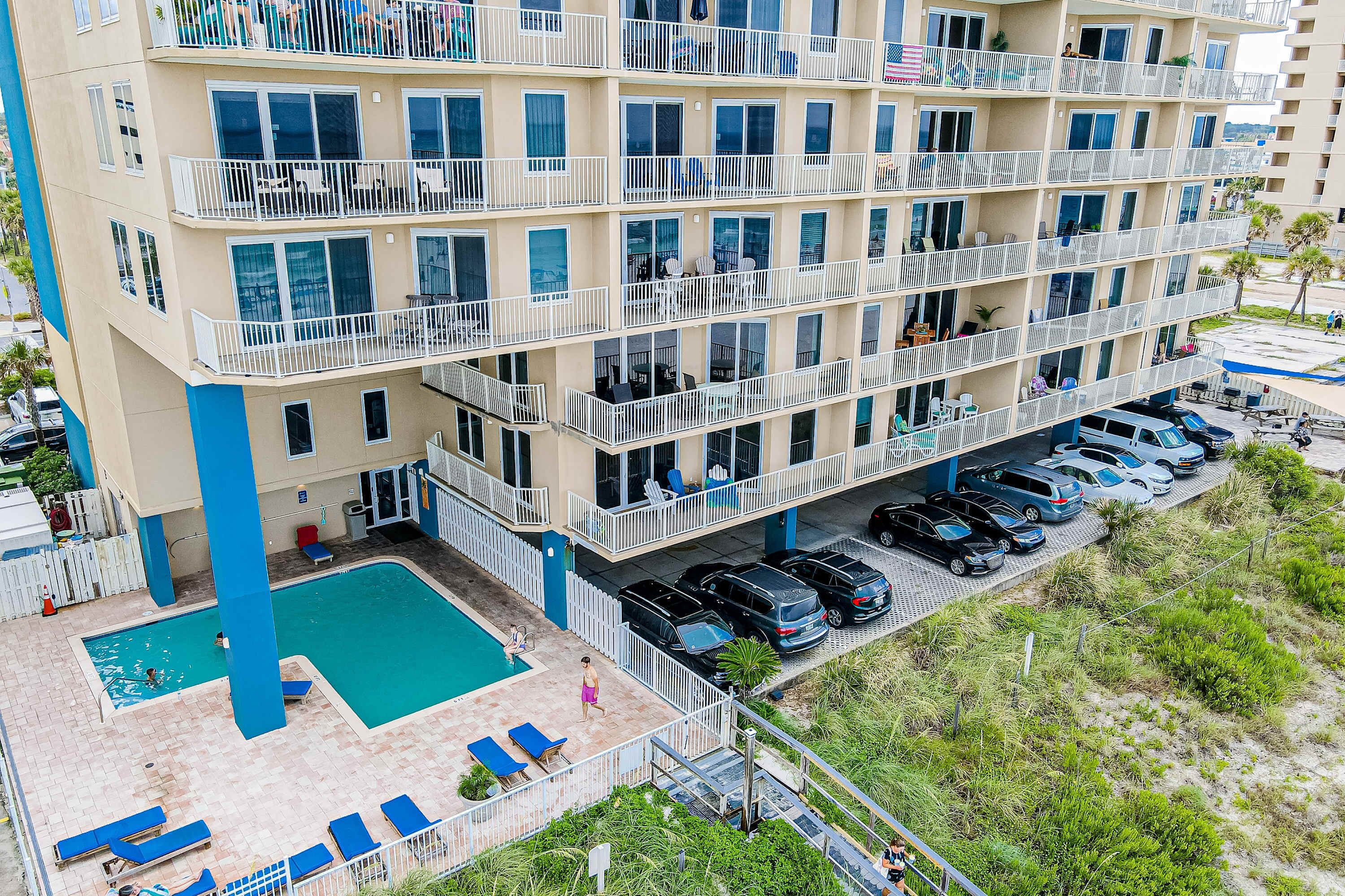 Un hotel de varios pisos con balcones, piscina y zona de estacionamiento.