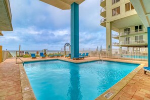 A pool area with blue lounge chairs, a tall blue pillar, and a view of a building with balconies. - Gulf-front condo with an incredible view off the balcony (Panama City Beach)