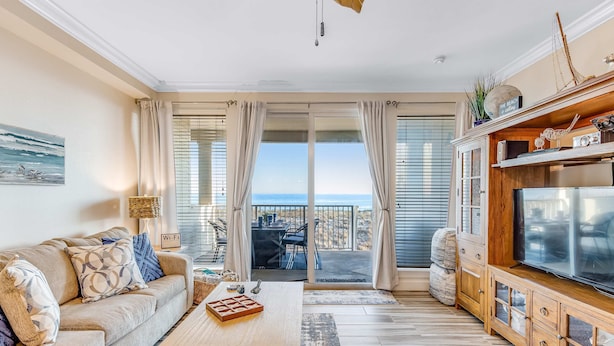 Ein Wohnzimmer mit Sofa, Couchtisch, Fernseher, Holzschrank und einem Balkon mit Meerblick.