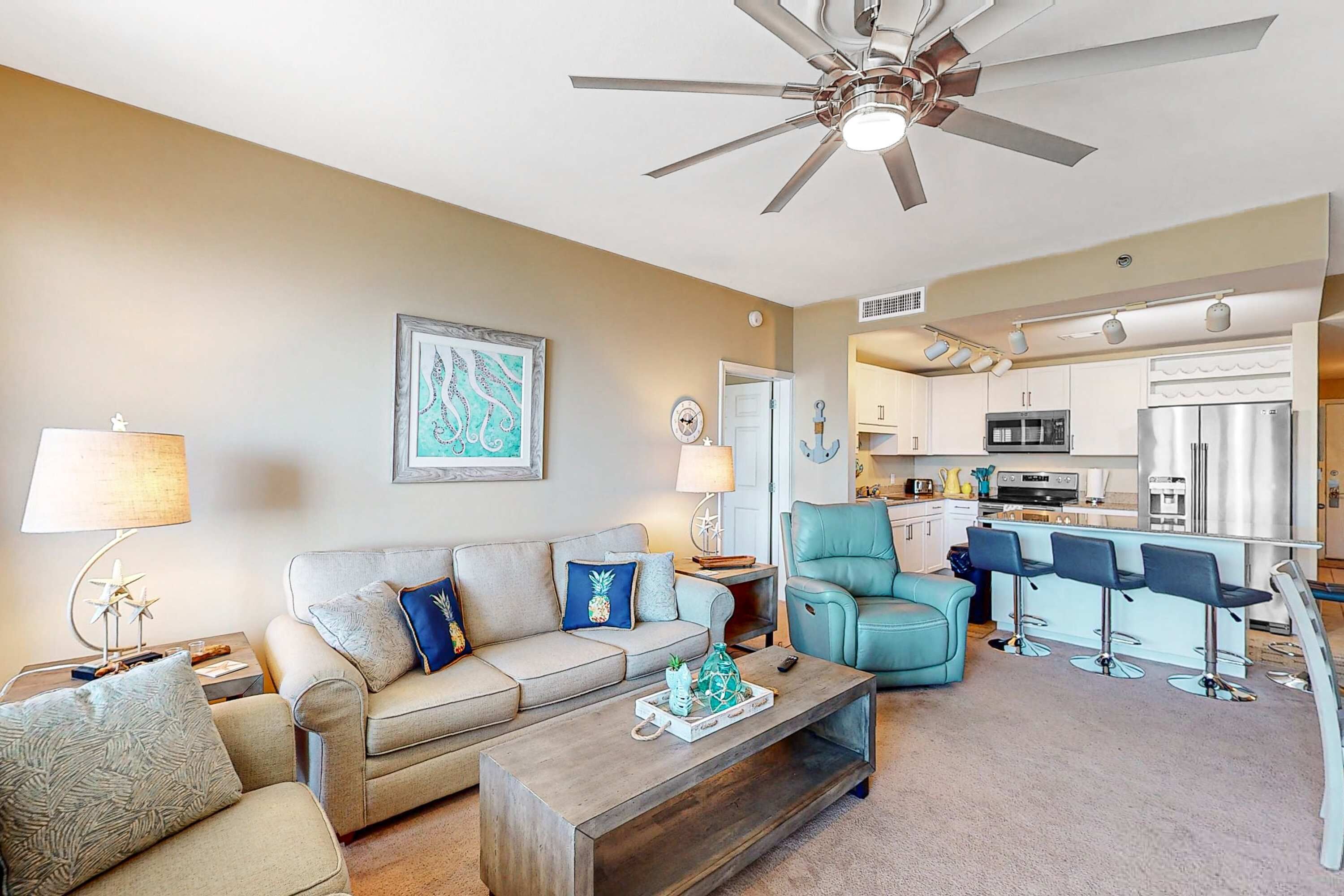 A living room with a sofa, coffee table, and a kitchen area with a bar and seating.