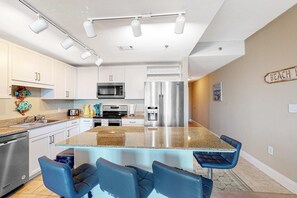 Una cocina moderna con armarios blancos, electrodomésticos de acero inoxidable y una encimera de granito. Hay taburetes azules en la isla y un microondas sobre la encimera.