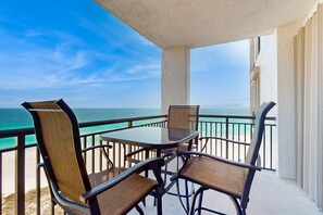 A balcony with a glass table and chairs, overlooking a beach and the ocean. - Gorgeous waterfront condo with pool, fitness room & WiFi (Navarre Beach)