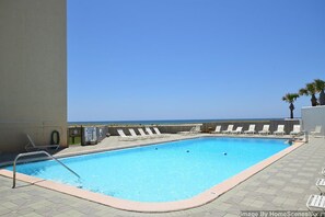 A rectangular pool with a clear blue water, surrounded by lounge chairs and a view of the ocean. - Gorgeous waterfront condo with pool, fitness room & WiFi (Navarre Beach)