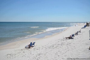 A beach with rows of blue beach chairs and umbrellas, a lifeguard tower, and a clear view of the ocean. - Gorgeous waterfront condo with pool, fitness room & WiFi (Navarre Beach)