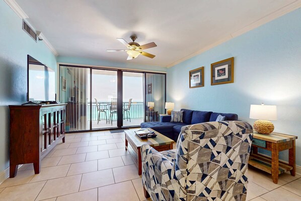 A living room with a sofa, armchair, coffee table, and a lamp. There is a sliding glass door leading to a balcony. - Gorgeous waterfront condo with pool, fitness room & WiFi (Navarre Beach)