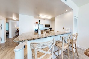 A modern kitchen with a granite countertop, stainless steel appliances, and wooden bar stools. - Tranquil escape in oceanfront complex near Pier Park with hot tub, pool & AC (Panama City Beach)