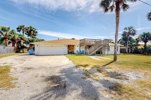 A two-story house with a garage, a covered patio, and a staircase leading to the upper floor. - Dog-friendly home steps to beach with 2 kitchens, dressing room & game room (Panama City Beach)