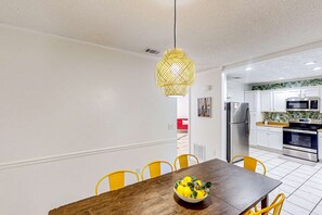A modern kitchen with white cabinets, stainless steel appliances, and a dining area with a wooden table and yellow chairs. - Dog-friendly home steps to beach with 2 kitchens, dressing room & game room (Panama City Beach)