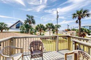 A wooden deck with two wicker chairs and a white plastic chair, overlooking a residential area with palm trees and houses. - Dog-friendly home steps to beach with 2 kitchens, dressing room & game room (Panama City Beach)