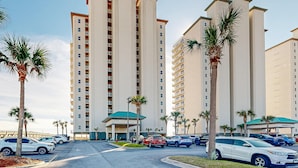A multi-story hotel with a central entrance, parking lot, and palm trees. - 7th-floor bright, open condo - close to dining with Gulf front views (Navarre Beach)