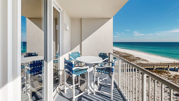 A balcony with a white table and blue chairs, overlooking a beach and ocean. - 7th-floor bright, open condo - close to dining with Gulf front views (Navarre Beach)