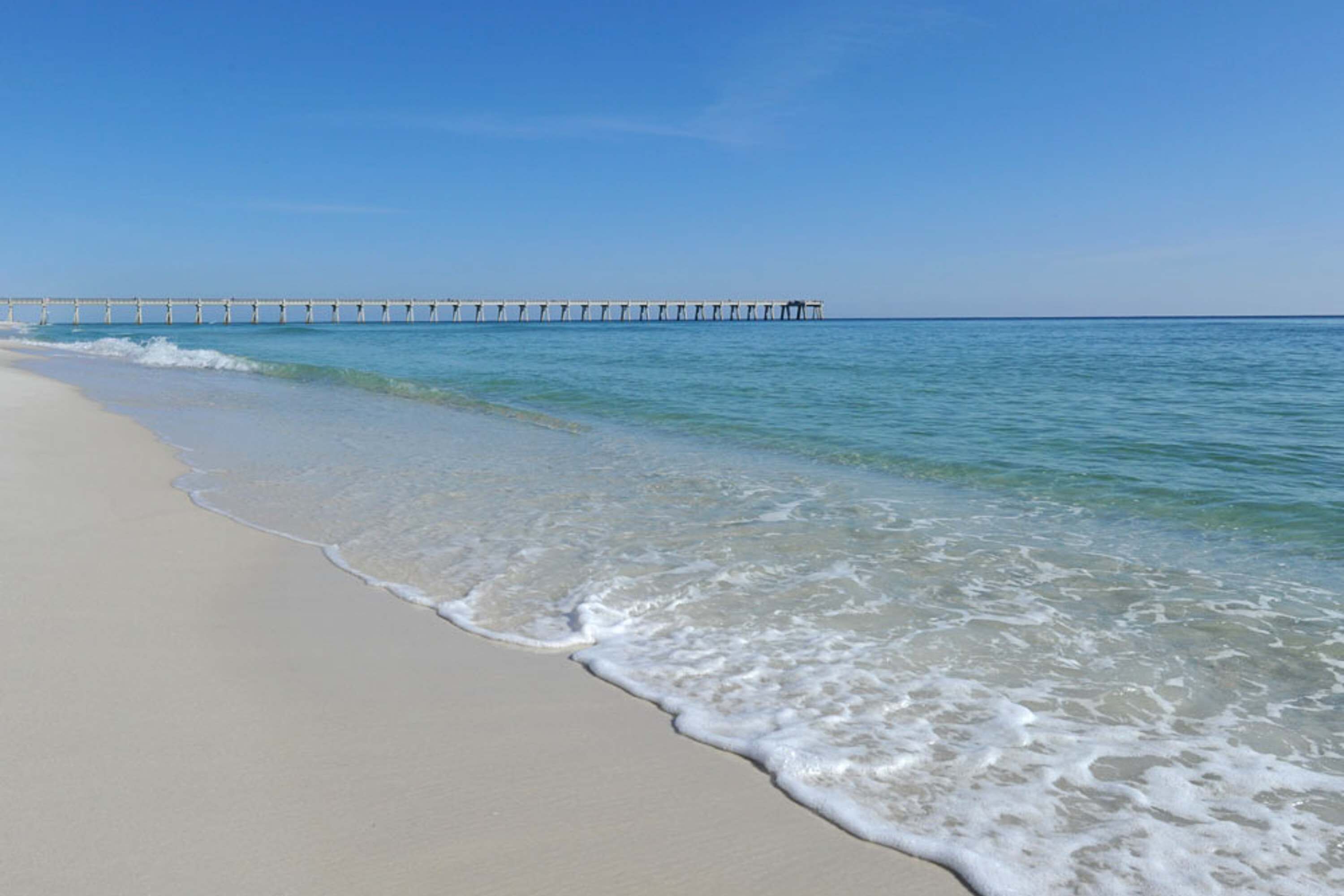 A beach with clear water and a pier extending into the sea.