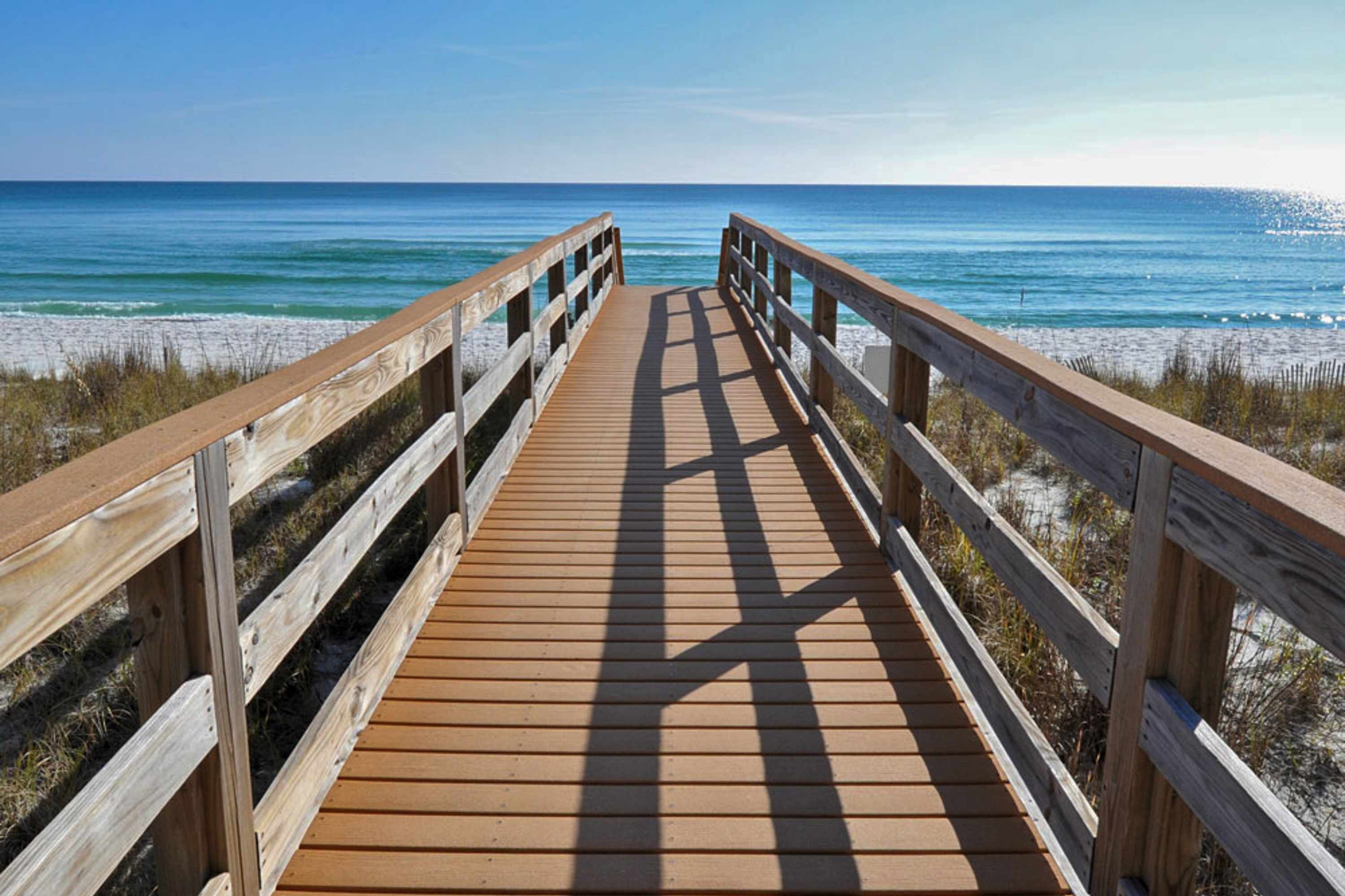 A wooden boardwalk leading to a beach with clear blue water and sandy shore.