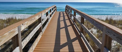 A wooden boardwalk leading to a beach with clear blue water and sandy shore.