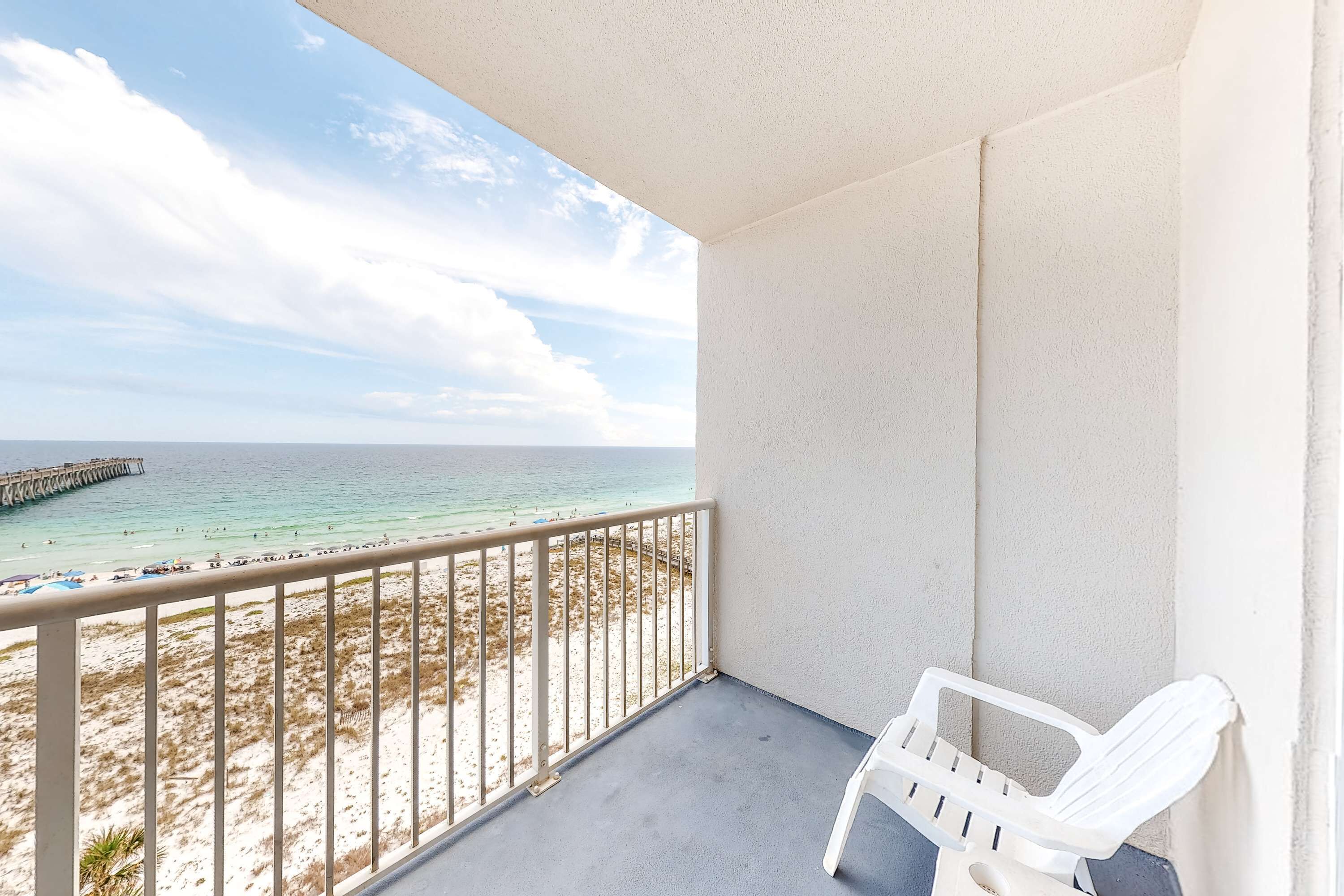 Een balkon met uitzicht op het strand en de oceaan, een witte stoel en een betonnen vloer.