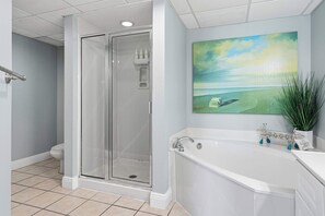 A bathroom with a glass shower enclosure, a bathtub, and a painting of a beach scene. - Beachfront Condo with gorgeous views, shared pool & beach access (Panama City Beach)