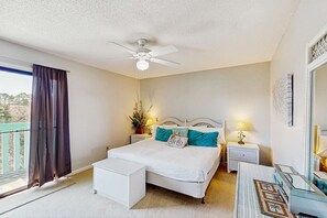 A bedroom with a bed, bedside tables, a ceiling fan, a window with curtains, and a view of the outdoors. - Relaxing retreat with Lake Powell views, dock access, 2 pools, & screened patio (Panama City Beach)