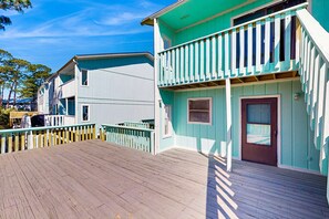 A wooden deck leading to a turquoise building with a balcony. - Relaxing retreat with Lake Powell views, dock access, 2 pools, & screened patio (Panama City Beach)