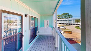 A balcony with a white bench, a door, and a view of a building and street. - Relaxing retreat with Lake Powell views, dock access, 2 pools, & screened patio (Panama City Beach)