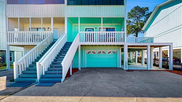 A two-story building with a turquoise garage door, white railings, and a concrete driveway. - Relaxing retreat with Lake Powell views, dock access, 2 pools, & screened patio (Panama City Beach)