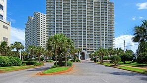 A large, multi-story hotel with a central entrance, surrounded by well-maintained landscaping and palm trees. - Inviting beach view condo with balcony, amazing pool, gym, & W&D (Miramar Beach)