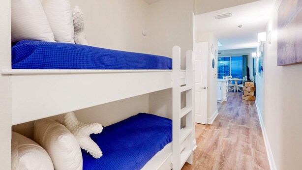A bunk bed with white and blue bedding, a white chair, and a wooden floor. - Inviting beach view condo with balcony, amazing pool, gym, & W&D (Miramar Beach)