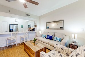 A modern living room with a sofa, coffee table, and a kitchen area in the background. - Inviting beach view condo with balcony, amazing pool, gym, & W&D (Miramar Beach)