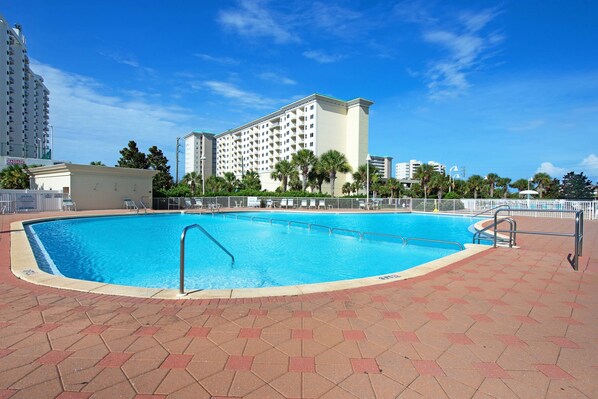 A swimming pool with a tiled deck, surrounded by palm trees and a large hotel building. - Inviting beach view condo with balcony, amazing pool, gym, & W&D (Miramar Beach)