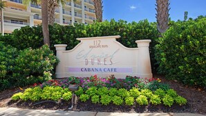 A sign for the Cabana Cafe at 112 Seascape Blvd., surrounded by lush greenery and palm trees. - Inviting beach view condo with balcony, amazing pool, gym, & W&D (Miramar Beach)